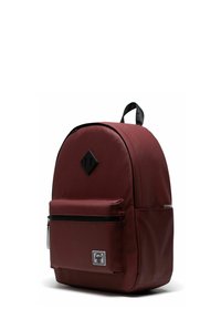 Sac à dos rouge foncé avec une poche zippée avant, une poignée noire sur le dessus, une poche latérale, et un patch logo noir en forme de diamant sur le panneau avant supérieur.