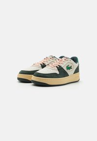 Lacoste sneakers with a beige leather and dark green suede upper, pink laces, and a cream midsole, featuring a green logo on the side.