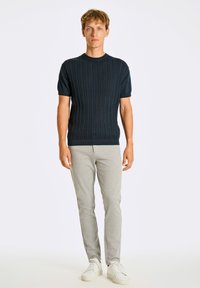 Granatowy sweter z krótkim rękawem, wykonany z dzianiny o teksturowanym prążkowanym wzorze, zestawiony z jasnoszarymi spodniami typu tapered i białymi sneakersami.