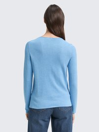 Lichtblauwe trui met lange mouwen en een ronde halslijn. Zachte, gestructureerde stof, ontworpen voor een aansluitende pasvorm, gecombineerd met donkerdenim jeans.