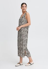Rochie cu un model negru și bej, cu fante laterale și bretele subțiri; modelul este asortat cu pantofi de culoare deschisă, având detalii cu cataramă.