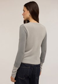 Ljust grå tröja med långa ärmar och en något mörkare grå accent på axlarna. Texturead stickad tyg. Sittande design.