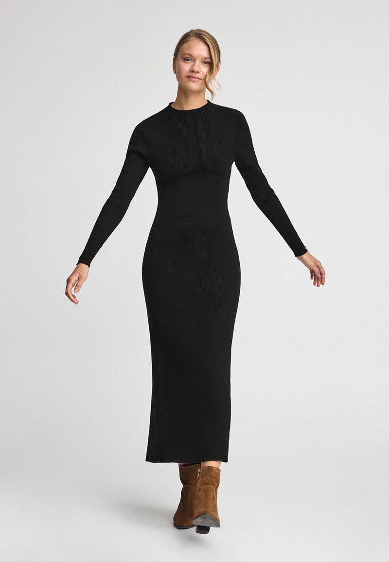 Svart ribbat stickat långärmat klänning med en åtsittande silhuett som sträcker sig ner till anklarna, tillsammans med bruna mockaankelboots.