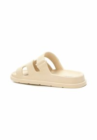 Sandalias beige de tipo slip-on con dos correas anchas y diseños recortados; hechas de un material suave y flexible; suela contorneada para mayor comodidad.