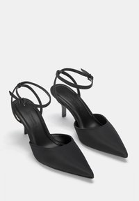 Črne čevlje s koničastim prstom iz gladkega materiala, ki imajo tanke gležnjske trakove in eleganten, nizek model pete.