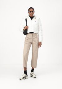 Hvit kort pufferjakke, beige skreddersydde bukser, svart turtleneck og mønstrete joggesko. Svart crossover-veske og solbriller.