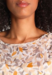 Blusa a fiori realizzata in tessuto leggero e trasparente, con tonalità tenui di giallo, marrone e grigio, dotata di scollatura ampia e texture a costine.