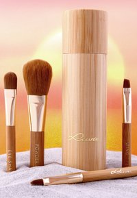 Bambus-Makeup-Pinselset mit vier Pinseln und einem zylindrischen Aufbewahrungsetui. Braune Borsten, metallische Akzente in Gold, gravierte Beschriftungen auf den Griffen.