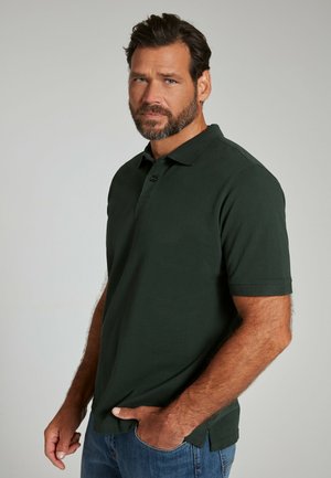 Polo shirt verde scuro in misto cotone, con patta a tre bottoni, maniche corte e spacchi laterali. Indossato con jeans blu.