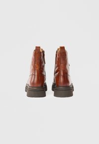 Par av brune lær ankle boots med tykke svarte såler, bakvinkel, med sidestropper og trekkbånd mot en enkel hvit bakgrunn.