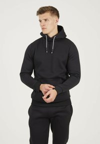 Sweat à capuche noir, avec cordons de serrage, poche kangourou et poignets côtelés. Texture lisse, design décontracté, coupe ajustée.