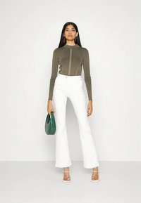 Maslinasto zelena majica s rebrastim uzorkom i dugim rukavima, s prednjim šavom, uparena s visokim strukom bijelim hlačama širokih nogavica i zelenom torbicom s teksturom. Prozirne sandale s trakicama.