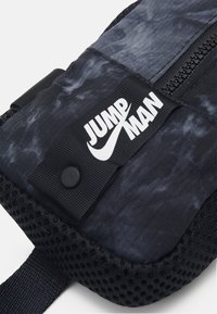 Zwarte en grijze textielen zak met een gaasbodem, voorzien van een opvallend wit "JUMP MAN" logo en een ritssluiting aan de bovenkant.