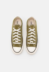 Oliwkowe tenisówki z tkaniny płóciennej, z białymi sznurowadłami, gumowymi noskami i czarną, kontrastującą podeszwą. Charakteryzują się przeszyciami i teksturowanym materiałem.