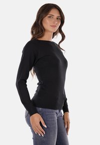 Maglione nero a maniche lunghe con un design aderente, scollo rotondo e polsini a coste. Texture liscia e morbida, mostrato con jeans blu.