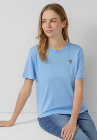 Lichtblauw katoenen t-shirt met korte mouwen en ronde hals, met een klein zwart hartje waarin het woord "LOVE" staat. Casual fit.