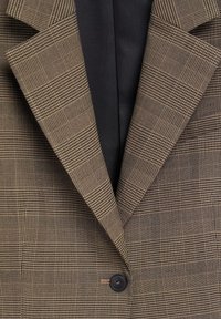 Blazer à carreaux marron avec col à revers en encoche et une fermeture à un bouton noir sur un vêtement intérieur foncé.