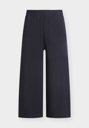 Μαύρο παντελόνι με φαρδιά μπατζάκια και ελαστική μέση, που πέφτει ίσια μέχρι τον αστράγαλο, σε απλό λευκό φόντο.