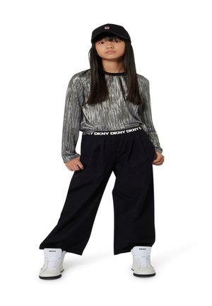 Top de manga larga a rayas plateadas con un cuello negro, combinado con pantalones sueltos negros que tienen una cinturilla con el logo de DKNY y zapatillas blancas de caña alta.