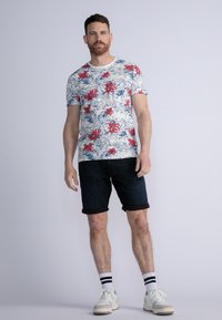 Camiseta de manga corta con cuello redondo que presenta un estampado floral con flores rojas sobre un fondo blanco. Combinada con pantalones cortos de mezclilla oscuros y remangados.