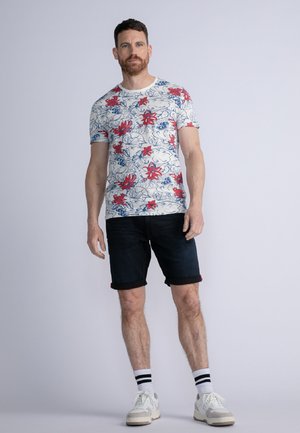 Tricou cu mânecă scurtă și guler rotund, cu un imprimeu floral cu flori roșii pe un fundal alb. Asortat cu pantaloni scurți din denim închis, răsuciți.