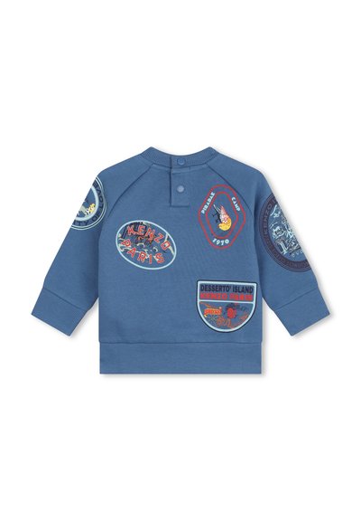 Sweatshirt bleu à manches longues, avec de multiples patches colorés et une fermeture à pression au cou. Texture douce, poignets et ourlet côtelés.