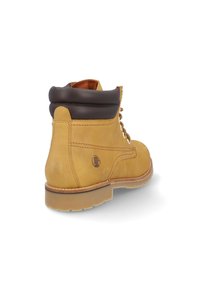 Bota de cuero amarillo con un collar acolchado marrón, ojales de metal y una suela de goma. Presenta un logotipo en el costado y costuras visibles.