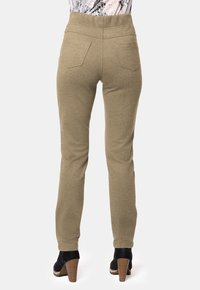 Pantalones elásticos beige con cintura alta, dos bolsillos traseros y un corte slim, combinados con botines negros de tacón.
