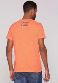 Camiseta de manga corta en naranja brillante, de mezcla de algodón, con un cuello redondo y texto negro impreso en la parte posterior. Diseño de ajuste casual.