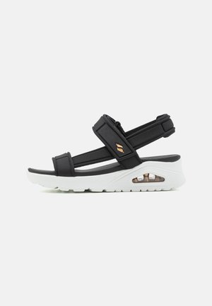 Sandal nero con cinturini regolabili, suola bianca e dettaglio di ammortizzazione ad aria. Realizzato in materiale sintetico, presenta una suola antiscivolo.