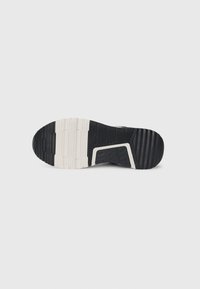 Sort og hvid gummisål af en sneakers, der viser slidbanemønstre og tekstur mod en hvid baggrund.