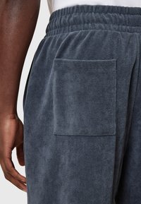 Grijze badstofbroek met een elastische tailleband en een rechthoekige patchzak aan de zijkant, die een zachte textuur en een casual ontwerp benadrukt.