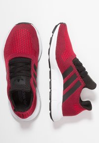 Röda mesh atletiska skor med svarta accenter och tre svarta ränder. Har en vadderad vit sula och en strukturerad svart tygtunga.