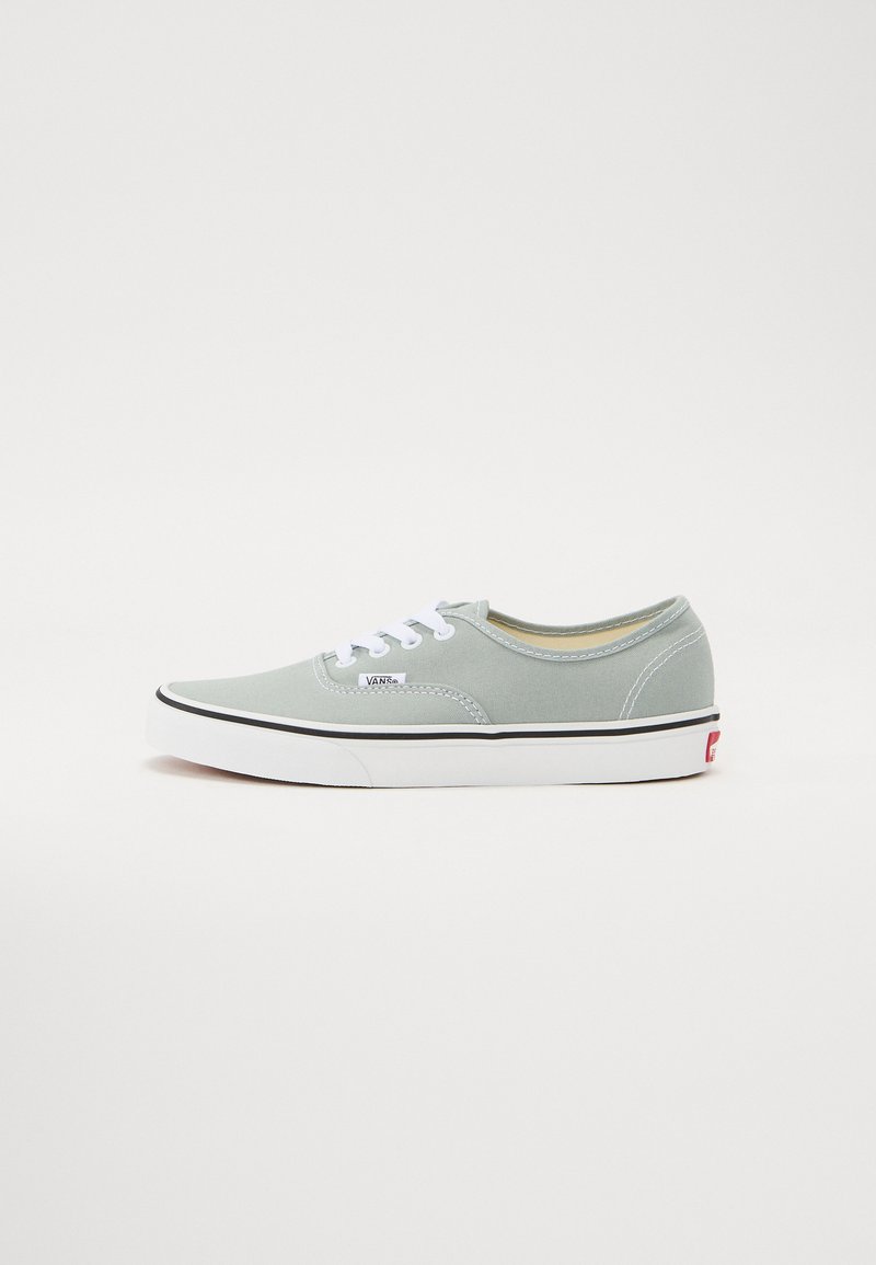 Ljusgrå canvas sneakers med vita snören, svart gummisula och en röd accentlogotyp på hälen. Rund tå och klassisk design.