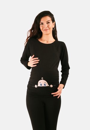 Schwarzes, langärmliges Stillshirt mit gerafften Seiten und einem Cartoon-Baby-Design, das aus dem Bauchbereich herauslugt. Weicher Stoff.