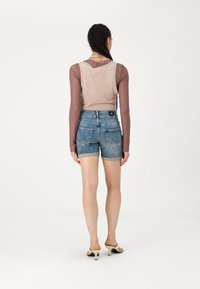 Top senza maniche color marrone chiaro sovrapposto a un top a maniche lunghe, abbinato a pantaloni corti in denim blu; i pantaloni corti presentano risvolti e tasche.