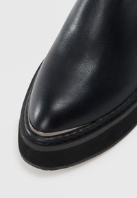 Melna ādas potītes zābaks ar smailu purngalu, gludu tekstūru, sudraba akcentu apdari un tumšas zamšas zoli. Klasisks un elegants dizains.