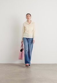 Un pull en tricot beige clair avec un col, un jean évasé bleu et un sac fourre-tout rose avec une doublure noire. Textures douces, coupe décontractée.
