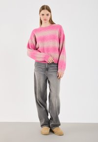 Maglione a righe rosa e beige, vestibilità oversize, con polsini a coste. Abbinato a jeans grigi sbiaditi e scarpe beige slip-on.