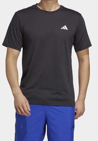 Man wearing a plain black Adidas short-sleeve t-shirt and bright blue Adidas athletic shorts against a plain background.