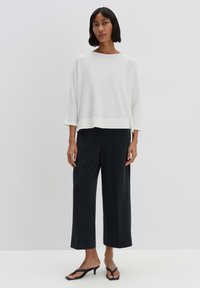 White ribbed sweatshirt with a boat neckline, paired with black wide-leg pants and sandals. Smooth texture, relaxed fit, and simple design.