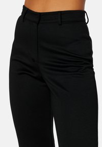 Černé tailored kalhoty vyrobené z hladké tkaniny, s přiléhavým pasem, předním záhybem a jemnými bočními detaily. Žádné viditelné kování.