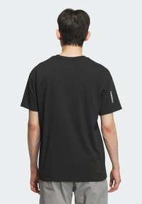 T-shirt en coton noir à manches courtes, col rond, avec un petit logo imprimé en blanc sur la manche gauche. Design simple et dépouillé.