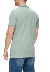 Jasnozielona koszulka polo wykonana z miękkiej tkaniny, z płaskim kołnierzykiem i krótkimi rękawami. Dół koszulki ma boczne rozporki, zestawiona z niebieskimi szortami dżinsowymi.