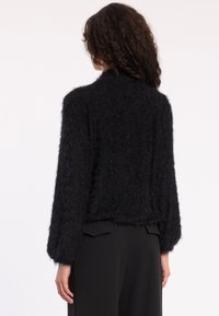 Schwarze, flauschige, strukturierte Strickjacke mit langen Ärmeln und kurzer Passform, ausgestattet mit einem runden Kragen und einer weichen Oberfläche.