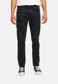 Jeans in denim nero con una vestibilità slim e design a cinque tasche. Cuciture a punto e cintura classica. Abbinati a sneakers nere e bianche.