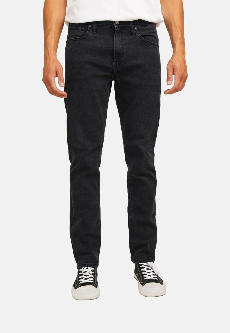 Jeans in denim nero con una vestibilità slim e design a cinque tasche. Cuciture a punto e cintura classica. Abbinati a sneakers nere e bianche.