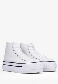 Sneakers alte bianche in tela con suola in gomma, strisce nere lungo il sottopiede e punte tonde con una finitura testurizzata.
