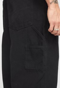 Pantalones cargo negros con múltiples bolsillos, fabricados en un material de algodón resistente y con costuras reforzadas para mayor durabilidad. Textura suave en toda su superficie.