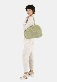 Geweven groene handtas met een ronde, gestructureerde vorm en een textuurfinish. Gecombineerd met een lichtbeige, gestreept outfit en witte hoge sandalen.